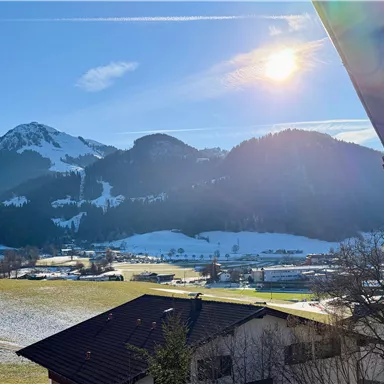 A picturesque winter landscape with snow-covered mountains and a clear blue sky. The sun shines over the gentle hills and the green meadows.