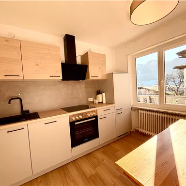 A modern kitchen with wooden cabinets and a compact design. The large window front provides plenty of daylight and a view of the outdoors.