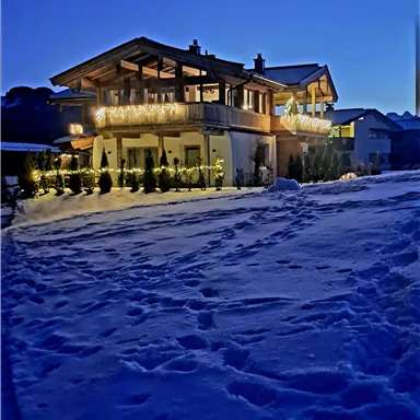 A beautiful wooden house with warm light in a snowy landscape. The sky is dark blue and there is fresh snow all around the house.