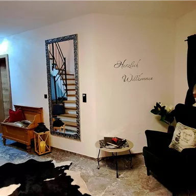 An inviting entrance area with a staircase, a black armchair, and a mirror on the wall. The walls are light, and there is space for plants and decorations.