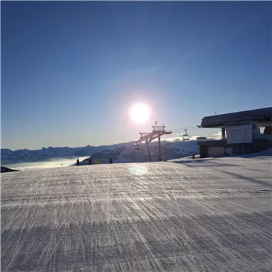 Ein sonniger Skitag auf einer glitzernden Piste. Im Hintergrund sind Skilifte und eine klare Berglandschaft zu sehen.