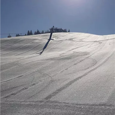 Eine verschneite Berge mit Skispuren und strahlendem Sonnenschein. Der Himmel ist klar und blau.