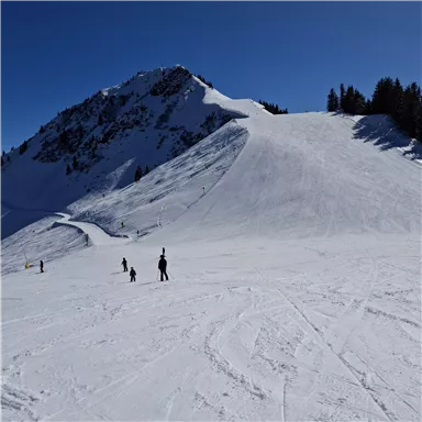 Eine verschneite Berglandschaft mit Skifahrern im Vordergrund. Der Himmel ist klar und blau.
