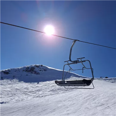 Ein Skilift schwebt über schneebedeckte Pisten unter einem klaren blauen Himmel. Die Sonne strahlt hell und sorgt für eine winterliche Atmosphäre.