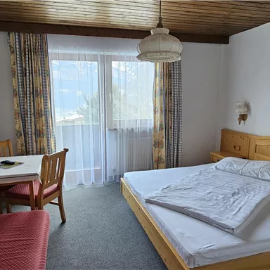 A cozy room with a large bed, a table and chairs. Large windows provide plenty of natural light.