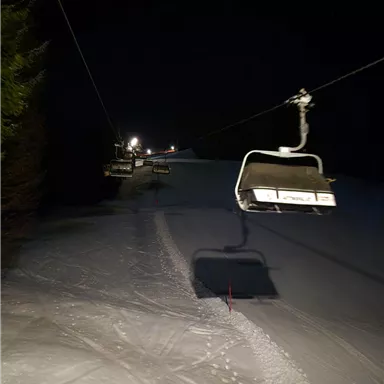 A ski lift facility at night on a snowy slope. The surroundings are dark, with few light sources in the distance.