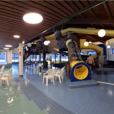 An indoor swimming pool with water slides and loungers. The room is bright and modernly designed.