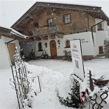 Ein charmantes, gut gebautes Haus im Alpenstil, umgeben von Schnee. Der verschneite Garten und die winterliche Stimmung verleihen dem Bild eine ruhige Atmosphäre.