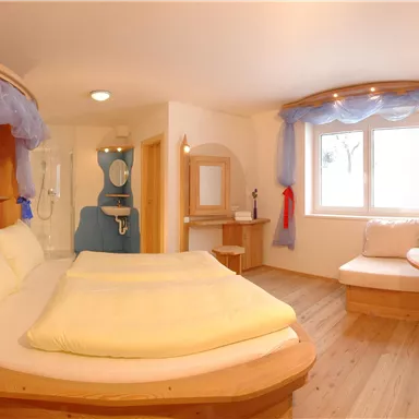 A cozy room with a round bed and wood paneling. The light is friendly, and there is a sitting area with a small table.