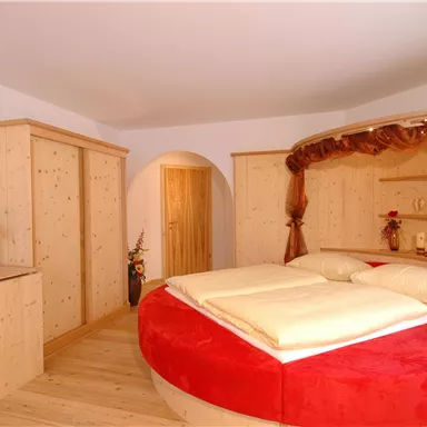 A cozy bedroom with a round bed and red accents. The furniture is made of light wood and creates a warm atmosphere.
