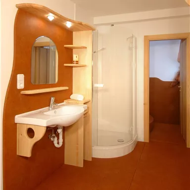 A modern bathroom with a sink, mirror, and shower cubicle. The walls are in warm colors and the floor is orange.
