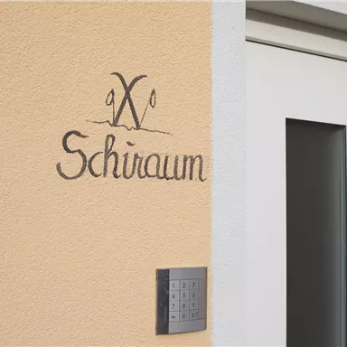 Ein Schild mit der Aufschrift "Schiraum" ist an einer orangefarbenen Wand angebracht. Daneben befindet sich ein modernes Eingangstürdesign.