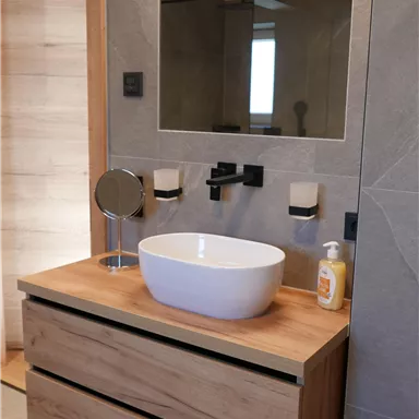 Ein modernes Badezimmer mit einem eleganten Waschbecken auf einem Holzmöbel. Der große Spiegel und die grauen Wände sorgen für ein stilvolles Ambiente.