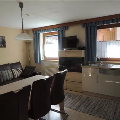 Eine gemütliche Wohnküche mit einem Esstisch und einer komfortablen Sofaecke. Die Fenster sind mit blauen Vorhängen ausgestattet und der Raum ist hell und einladend.