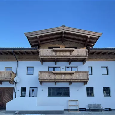 Ein modernes, zweigeschossiges Haus im alpinen Stil mit Holzbalustraden. Der Himmel ist klar und blau, und der Boden ist mit Schnee bedeckt.