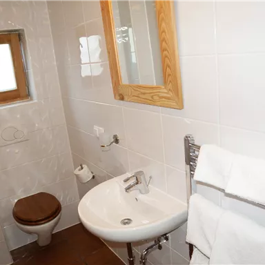 Ein modernes Badezimmer mit weißen Fliesen und einer Holzfensterrahmen. Es verfügt über ein Waschbecken, eine Toilette und Handtücher.