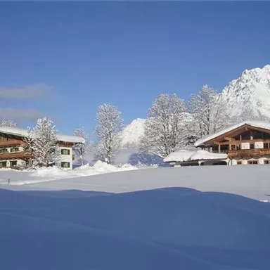 Eine schöne winterliche Landschaft mit schneebedeckten Hütten und hohen Bergen im Hintergrund. Der klare blaue Himmel vervollständigt die idyllische Szene.