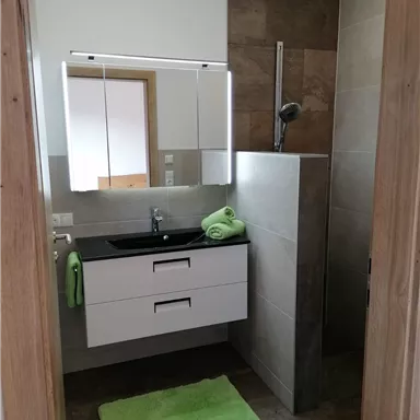 A modern bathroom with a shower and a sink. Green towels and a bath mat add color to the space.