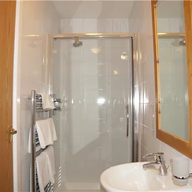 Ein helles Badezimmer mit einer Dusche und einem Waschbecken. An der Wand hängen Handtücher, und ein Spiegel ist vorhanden.