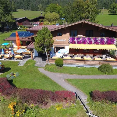 A cozy restaurant with blooming flowers and outdoor seating. Surrounded by a beautiful landscape with green grass and trees.