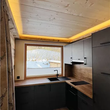 Eine moderne Küche mit einem Holzdekor und einem großen Fenster. Sanfte Beleuchtung an der Decke schafft eine einladende Atmosphäre.