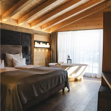 A modern bedroom with wooden ceilings and a large window. The room includes a bed, a bathtub, and a stylish decor.