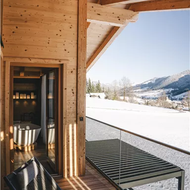 A modern wooden terrace with a view of snow-covered mountains. The decor is cozy and inviting.
