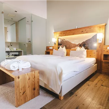 A cozy room with a large bed and wooden details. The bright ambiance creates a relaxing atmosphere.
