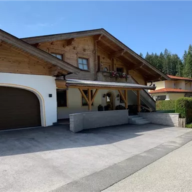 Ein gemütliches Haus im sogenannten Alpenstil mit Holzelementen. Der Eingangsbereich ist freundlich gestaltet und es gibt eine gepflasterte Auffahrt.