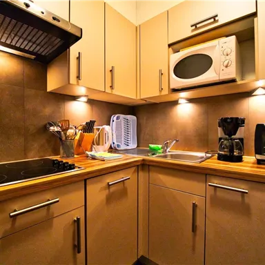 Eine moderne Küche mit Holzarbeitsfläche und umfangreicher Ausstattung. Die Küche verfügt über Kochfeld, Mikrowelle, und Kaffeemaschine.