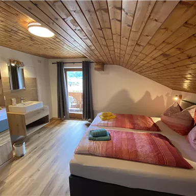 A cozy bedroom with two beds and a wooden wall. There is a window with a view and modern furniture.