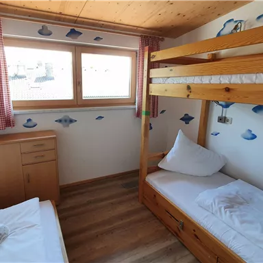 Ein gemütliches Schlafzimmer mit einem Etagenbett und einem Einzelbett. Die Wände sind mit Wolkenmotiven dekoriert und es gibt große Fenster für ausreichend Tageslicht.
