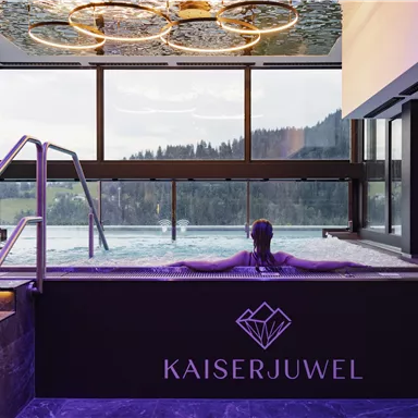 Ein modern gestalteter Wellnessbereich mit einem Pool und großen Fenstern. Im Vordergrund entspannt eine Person im Wasser.