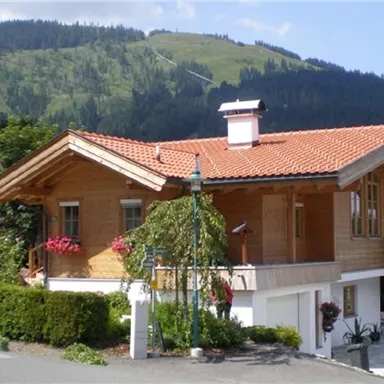 A traditional wooden house with a red roof and a beautiful flower view. In the background, green hills and mountains can be seen.