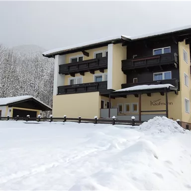 Ein gemütliches Gebäude im winterlichen Schnee, umgeben von verschneiten Bäumen. Der Himmel ist grau und neblig, was eine ruhige Atmosphäre schafft.