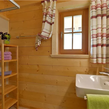 A modern bathroom with wood paneling. There is a shower, a sink, and a shelf cabinet with towels.