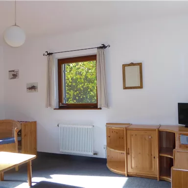 A bright living room with wooden furniture and a window that lets in light. There is a table, chairs, and a television.