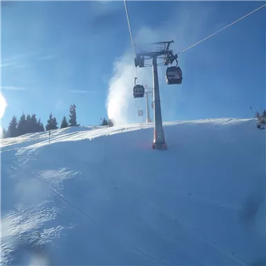 Eine Wintersportlandschaft mit frisch präparierten Pisten und einer Seilbahn. Der Himmel ist klar und blau, und der Schnee glitzert in der Sonne.