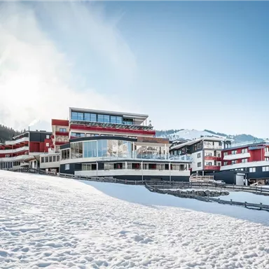 A modern hotel building in a snowy landscape. In the background, mountains and a clear blue sky are visible.