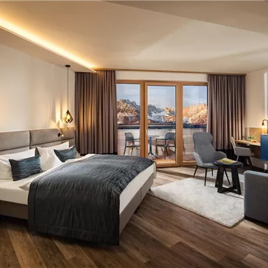 A modern hotel room with a large bed and elegant furnishings. Large windows offer a view of the landscape outside.