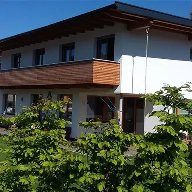 Ein modernes Haus mit einem eleganten Holzbalustrade und einem großen Garten. Die Umgebung ist grün und lädt zum Entspannen ein.
