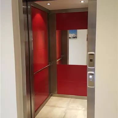 A modern elevator with red walls and shiny metal cladding. The elevator is open and ready for passengers.