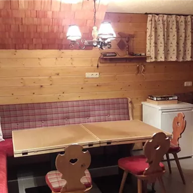 Ein gemütlicher Raum mit Holzverkleidung und einer Sitzecke. Der Tisch ist in der Mitte und es gibt eine kleine Küche mit Kühlschrank.