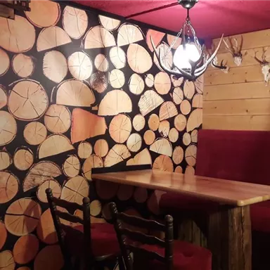 Ein gemütlicher Gastrobetrieb mit rustikaler Holzoptik. Die Wände sind mit Holzscheiben dekoriert, und die Sitzbereiche laden zum Verweilen ein.