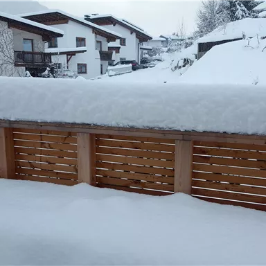 A wintry landscape with plenty of snow in front of a window. In the background, houses and snow-covered hills can be seen.