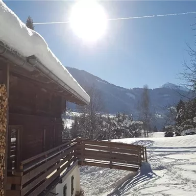 A cozy mountain cabin with a woodpile in the foreground. In the background, a snowy landscape stretches beneath a clear blue sky.