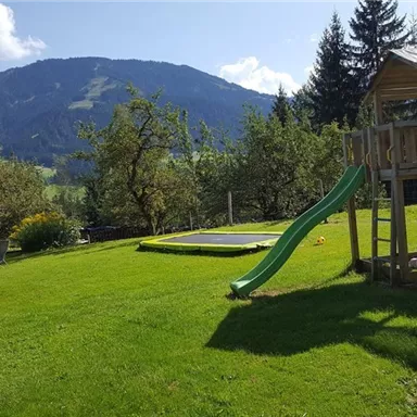 A beautiful garden with a playground structure and a slide. In the background, green hills and trees can be seen.