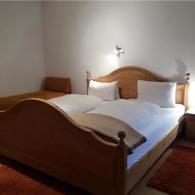 A cozy bedroom with a large wooden bed and a comfortable single bed. The room has a warm atmosphere and a carpet in orange.