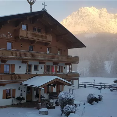 A beautiful chalet in winter, surrounded by snow and mountains. The facade of the house is made of wood and the atmosphere is calm and picturesque.