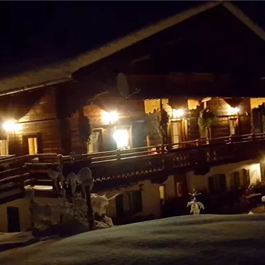 A cozy chalet in the snow, illuminated by warm light. The surroundings are quiet and wintry.